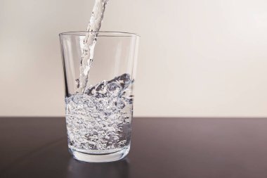 Masanın üzerinde bir bardak, bir su akıntısı aktif olarak dökülür, kabarcıklar oluşturur.