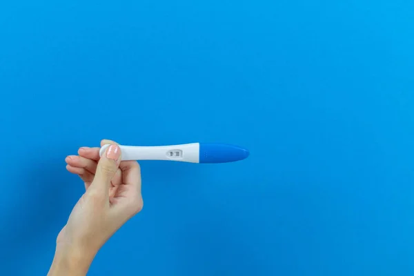 Mavi arka planda bir kızın ellerinde pozitif hamilelik testi.