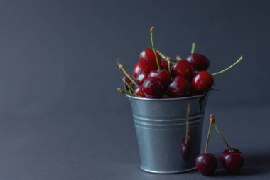 Koyu arkaplanda bir kovada kiraz, meyve mevsimi