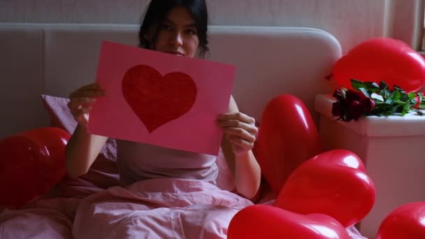 Ein junges Mädchen zeigt ein rotes Herz auf Papier. Valentinstag am Morgen. — Stockvideo