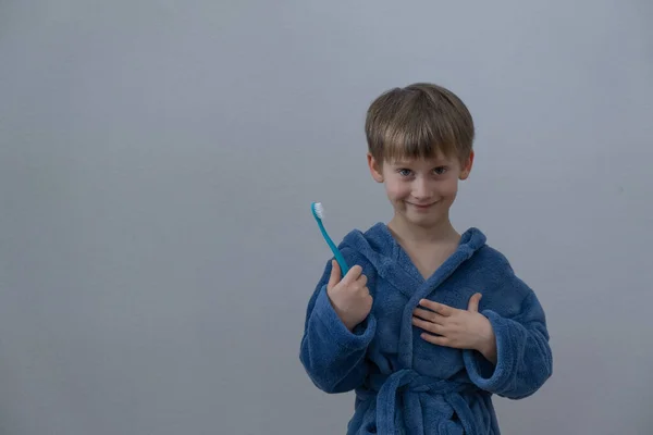 Un niño con una bata azul sostiene un cepillo de dientes en sus manos. —  Fotos de Stock