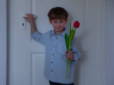 Beyaz kapının yanında elinde lale olan bir çocuk. Anneler günün kutlu olsun.
