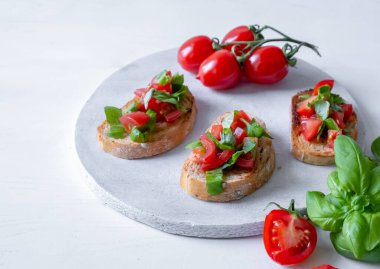Domatesli üç bruschetta ve beyaz tahta üzerinde taze fesleğen.