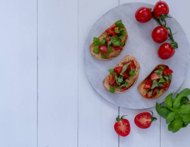 Domatesli üç bruschetta ve beyaz tahta üzerinde taze fesleğen.