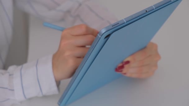 Woman sitting at her desk writes and uses pen with a digital tablet computer. — Video