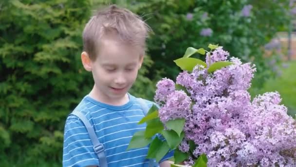 Menino loiro feliz com buquê de lilás no jardim em casa — Vídeo de Stock