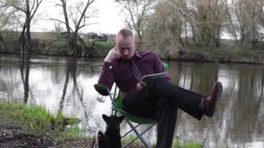 İşadamı oturan ile bir düşünme, Tablet ve çalışma için kamp için nehir tarafından zorlanır