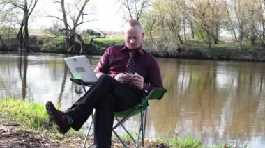 İşadamı oturan ile bir Tablet ve iş için kamp için nehir tarafından zorlanır