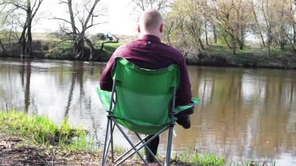 Empresario sentado con una tableta y se ve obligado a trabajar para acampar junto al río — Vídeo de stock