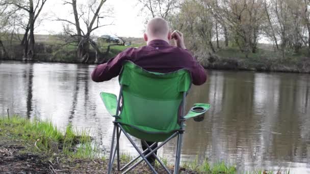 Uomo d'affari seduto dietro con una tavoletta ed è costretto a lavorare per il campeggio sul fiume — Video Stock