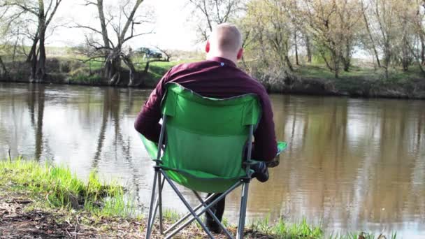 Empresario sentado de espaldas con una tableta y obligado a trabajar para acampar junto al río — Vídeo de stock