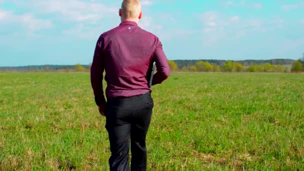 Empresario cansado caminando en el campo con el portátil — Vídeo de stock