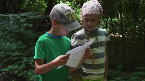 Geocaching - een jongen en een meisje het lezen van een vel papier met de baan in het bos — Stockvideo