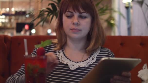 Fiatal nő ül egy kávézó: ivás eper koktél-egy tányérra, keres információkat, Online, beszél a telefonon — Stock videók