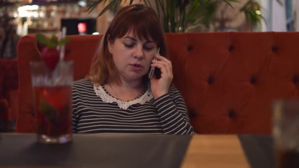 Νεαρή γυναίκα που κάθεται σε ένα Cafe: πίνοντας κοκτέιλ φράουλας σε ένα πιάτο που αναζητούν πληροφορίες σε απευθείας σύνδεση, να μιλάει στο τηλέφωνο — Αρχείο Βίντεο