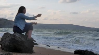 Genç kadın Rocky kıyısında oturan su içine taş ve özlüyor atma. Güçlü dalgalar dayak kayalara karşı