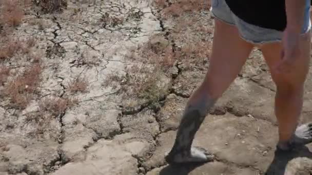 Женщина с ногами в грязи идет по пустынной дороге — стоковое видео