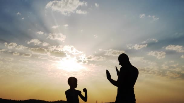 Mann trainiert mit einem Jungen eine Boxstunde. Silhouetten. — Stockvideo