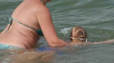 Anne kızı denize yüzmeyi öğretiyor.