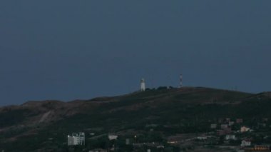 Deniz feneri günbatımı sırasında köyün tepede yanıp sönen Timelapse