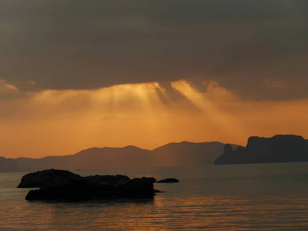 Güneş bulutların arkasından yükseliyor ve uzakta küçük bir tekne, Tayland, Krabi