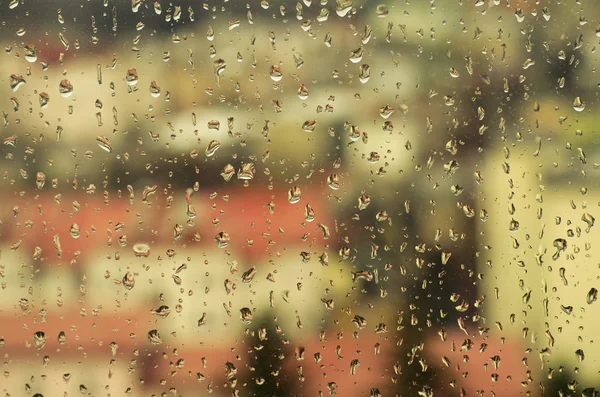 Uitzicht op de stad door een raam met regen druppels — Stockfoto