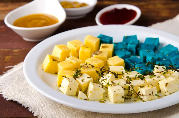 Prato de queijo, Gouda, feta, queijo pesto azul no prato branco com ervas, azeite, romã e molhos de mostarda — Fotografia de Stock