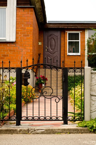 Red house facade with iron fence, green trees and flowers