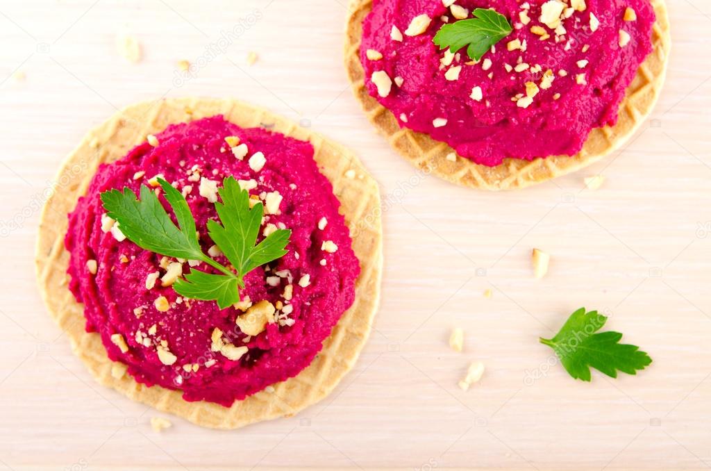 Beet hummus with peanuts and parsley on thin wafers