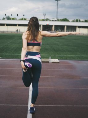 Genç bir kadın spor için stadyuma koşuyor, esniyor, su içiyor.