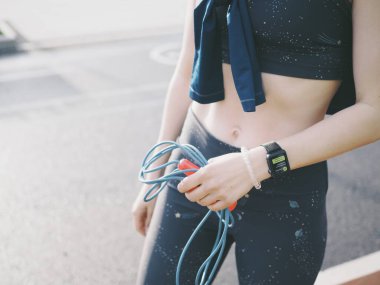 Genç bir kadın spor için stadyuma koşuyor, esniyor, su içiyor.