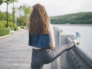 Genç bir kadın spor için stadyuma koşuyor, esniyor, su içiyor.