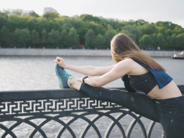 Genç bir kadın spor için stadyuma koşuyor, esniyor, su içiyor.