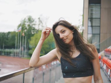 Genç bir kadın spor için stadyuma koşuyor, esniyor, su içiyor.