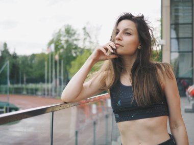 Genç bir kadın spor için stadyuma koşuyor, esniyor, su içiyor.