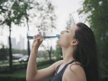 Genç bir kadın spor için stadyuma koşuyor, esniyor, su içiyor.