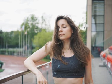 Genç bir kadın spor için stadyuma koşuyor, esniyor, su içiyor.