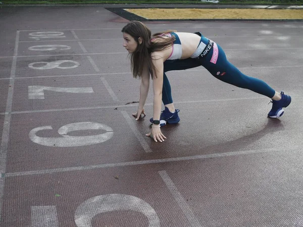 Genç bir kadın spor için stadyuma koşuyor, esniyor, su içiyor.