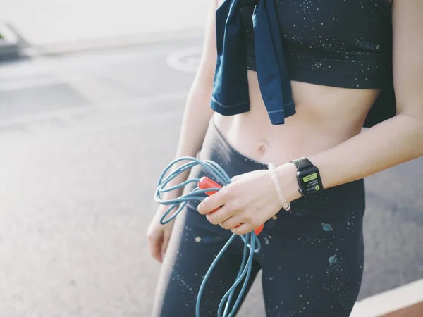 Genç bir kadın spor için stadyuma koşuyor, esniyor, su içiyor.