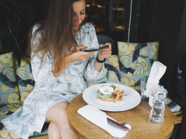 Genç bayan bir kafede telefon kullanıyor. Yemek fotoğrafları çekip telefonda konuşuyorlar.