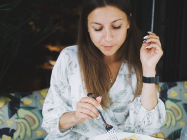 Genç bir kadın yazın verandada bir kafede yemek yiyor.