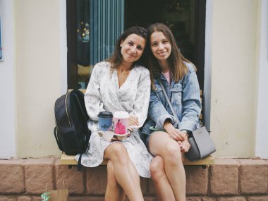 Kız arkadaşlar verandada oturur ve kameraya bakarlar.