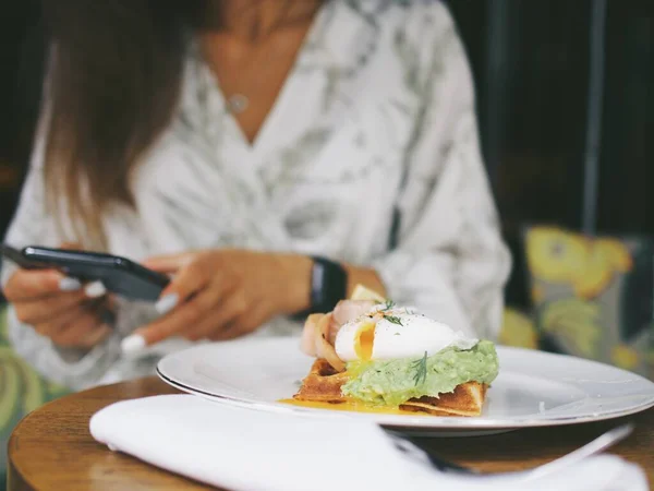 Genç bayan bir kafede telefon kullanıyor. Yemek fotoğrafları çekip telefonda konuşuyorlar.