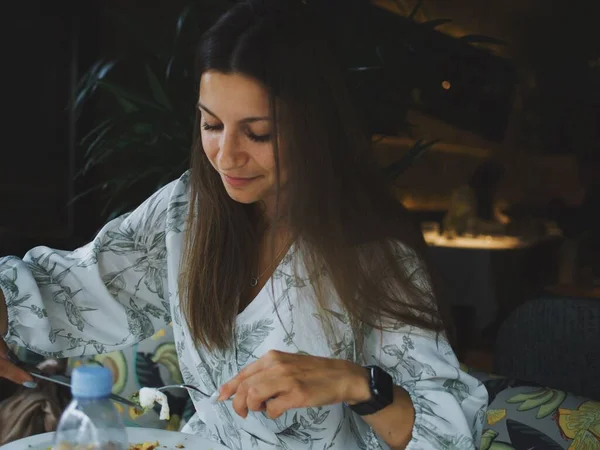 Genç bir kadın yazın verandada bir kafede yemek yiyor.