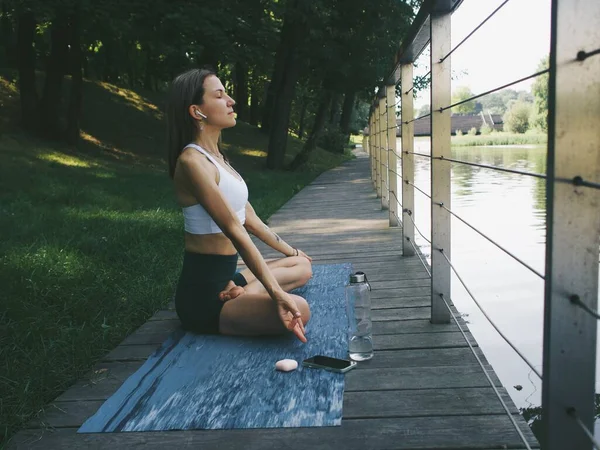 Genç bir kadın parkta meditasyon yapıyor ve yoga yapıyor.