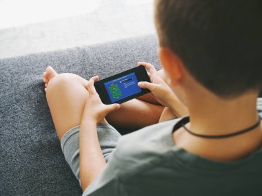 Çocuklar telefon ve tabletle bilgisayar oyunu oynar ve kulaklıklarla otururlar.