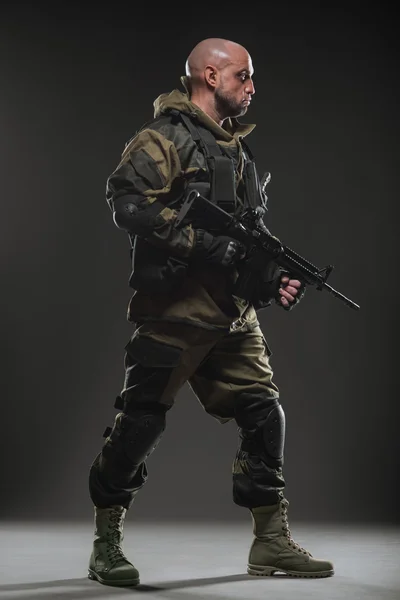 Soldato uomo tenere mitragliatrice su uno sfondo scuro — Foto Stock