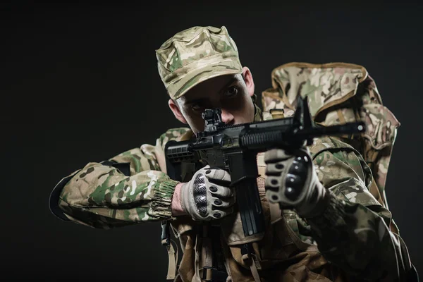 Soldado hombre mantenga ametralladora sobre un fondo oscuro — Foto de Stock