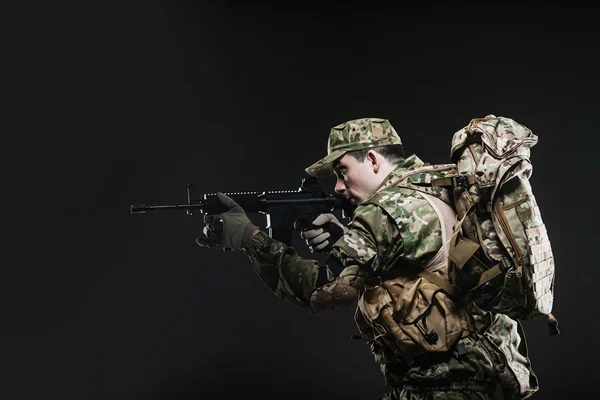 Soldado hombre mantenga ametralladora sobre un fondo oscuro — Foto de Stock