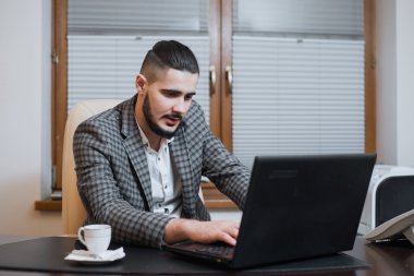 genç yakışıklı işadamı dizüstü bilgisayarda kahve molası sırasında ofiste çalışıyor.